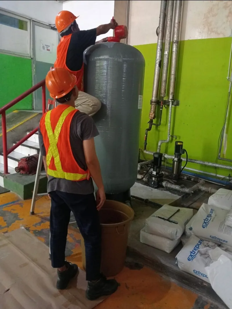Water & Wastewater Treatment — Pemasangan water softener — pengisian media resin ke vessel FRP di ruang utilitas pelanggan